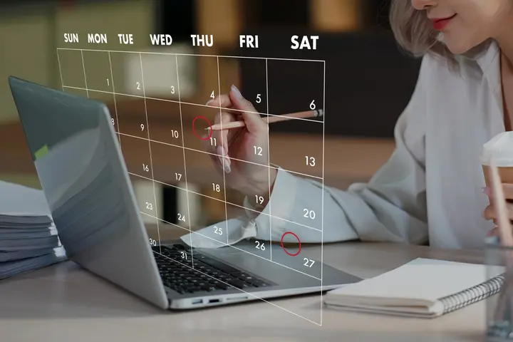 Woman circling dates on a calendar in front of a laptop