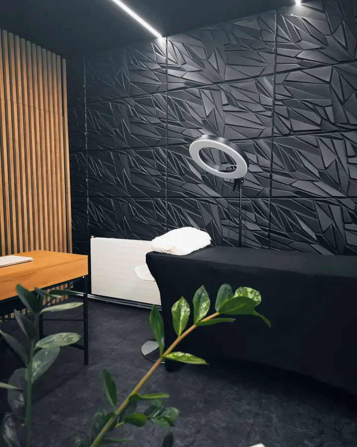 Ring light against black 3D wall panels, with a plant in the foreground